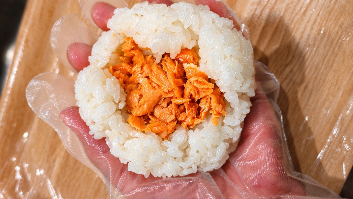 ほぐした紅鮭を白いごはんで包み、手で握っているところ