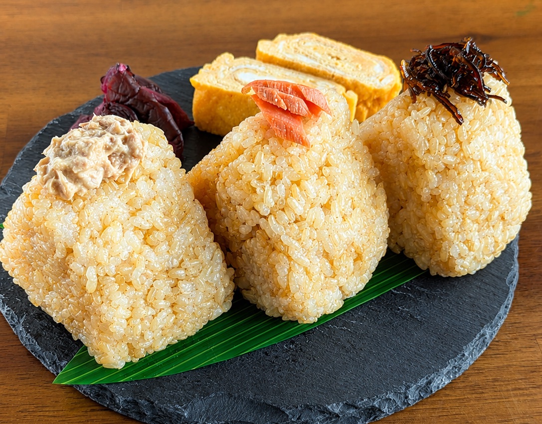 玄米で握ったおむすび3種 — 石のプレートに並んだツナマヨ・紅鮭・昆布のおむすび