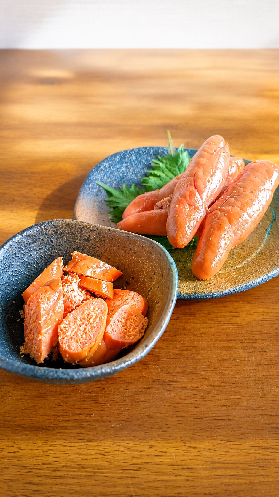 器に盛った生のたらこと、皿に並べた一腹のたらこ — 淡い橙色で、粒がきめ細かい